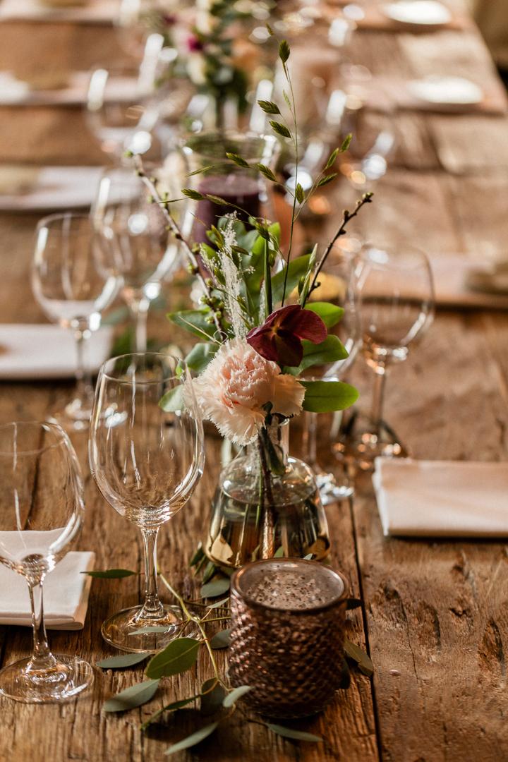 Elegante Tischdekoration mit Blumen, Kerzen und Weingläsern auf einem rustikalen Holztisch im Hofgut Maisenburg.