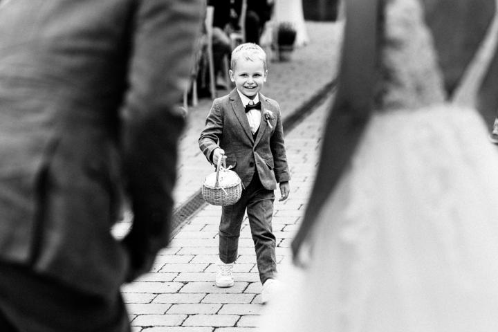 Kleiner Junge im eleganten Anzug bringt dem Brautpaar die Ringe während der freien Trauung in der Oase Weil, lächelnd und mit einem Körbchen in der Hand.